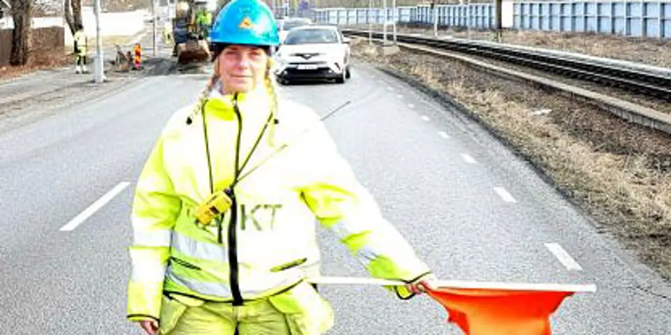 Bild på kvinna som håller en vaktflagga på en trafikerad väg